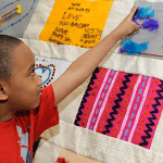 Young Boy Placing Feathers on Fabric Art Piece